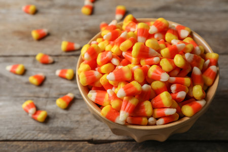 Bowl with tasty candy corns on wooden table. Space for text