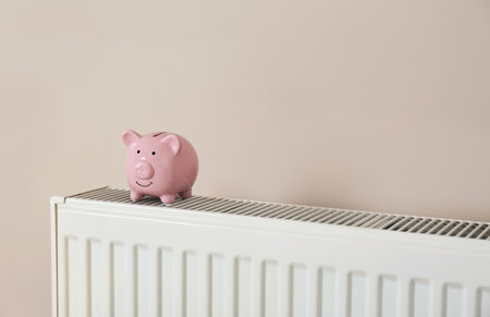 Piggy bank on heating radiator against light backgroundの写真素材