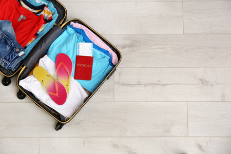 Packed suitcase with summer clothes and passport on wooden background, top view. Space for text