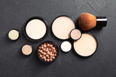Flat lay composition with various makeup face powders on dark background