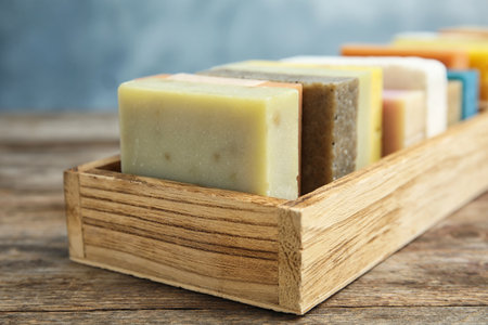 Many different handmade soap bars in wooden box on table, closeup