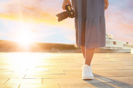 Young female photographer with professional camera in sunset lights at pier. Space for text