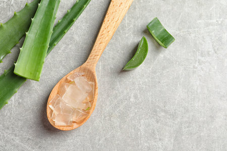 Flat lay composition with spoon of peeled aloe vera, green leaves and space for text on gray backgroundの写真素材