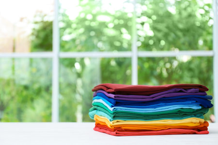 Stack of bright folded clothes on table against blurred background. Space for textの写真素材