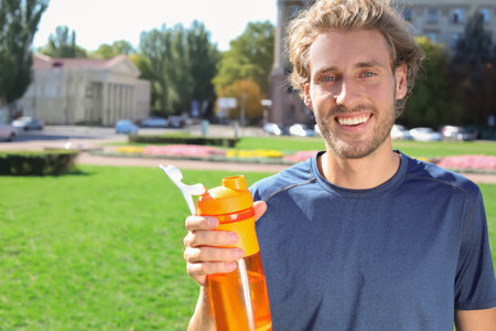 Young man holding bottle with clean water on city street. Space for textの写真素材