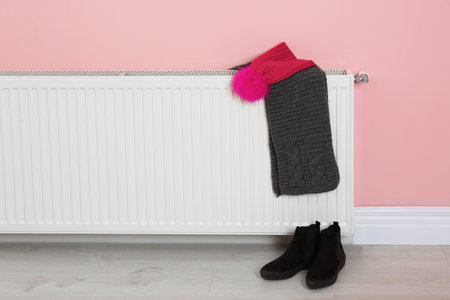 Heating radiator with knitted cap, scarf and shoes near color wallの写真素材