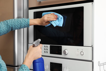 Woman cleaning oven with rag in kitchenの写真素材