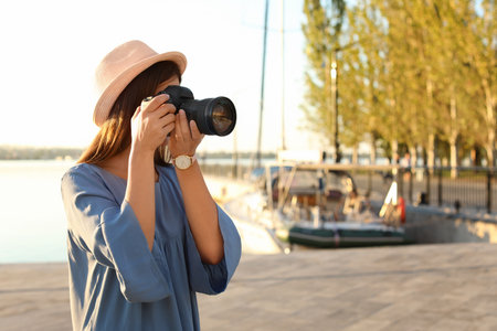 Young female photographer taking photo with professional camera at pier. Space for textの写真素材