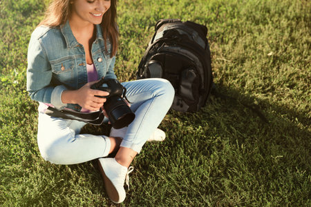 Young female photographer holding professional camera and sitting on grass outdoorsの写真素材
