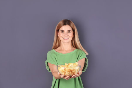 Woman with bowl of potato chips on gray backgroundの写真素材