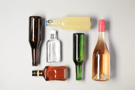 Bottles with different alcoholic drinks on light background, top view