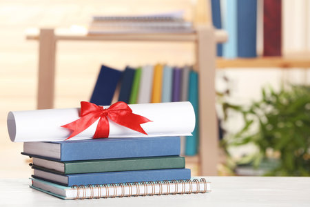 Graduate diploma with books and notebook on table against blurred backgroundの写真素材