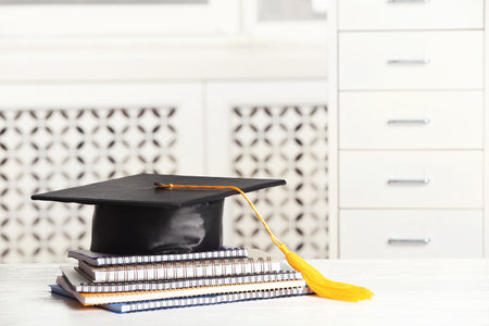 Graduation hat with notebooks and notebooks on table against blurred background. Space for textの写真素材