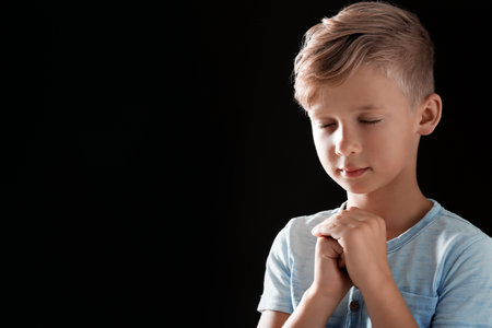Little boy with hands clasped together for prayer on black background. Space for textの写真素材