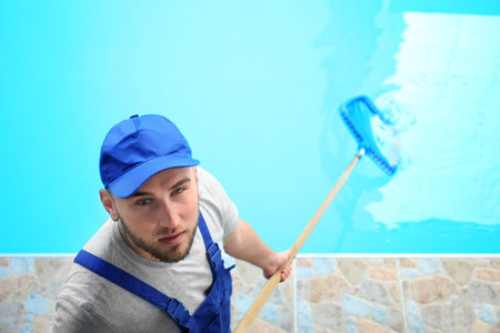 Male worker cleaning outdoor pool with scoop netの写真素材