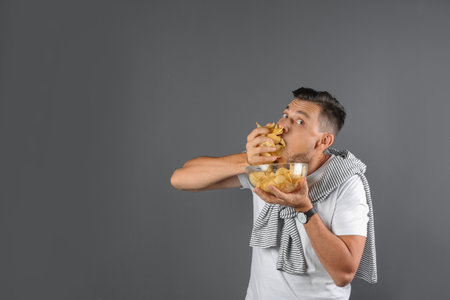 Man eating potato chips on gray background. Space for text