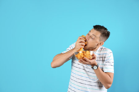Man eating potato chips on color background. Space for textの写真素材