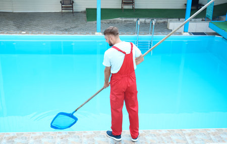 Male worker cleaning outdoor pool with scoop netの写真素材