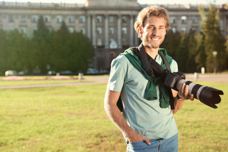 Handsome male photographer holding professional camera on street. Space for textの写真素材