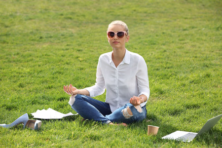 Young woman meditating on green lawn in park. Joy in the momentの写真素材