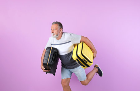 Senior man with suitcases running on color background. Vacation travelの写真素材