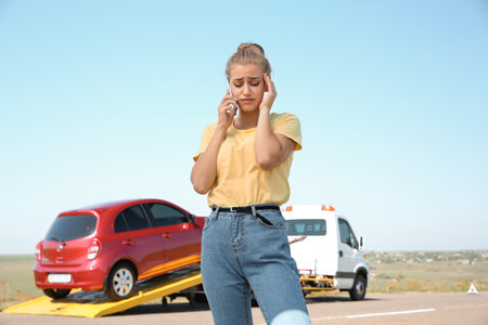 Woman talking on phone near tow truck with broken car outdoorsの写真素材
