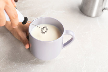 Woman using milk frother in cup on tableの写真素材