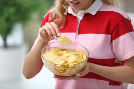 Woman with bowl of potato chips on blurred background, closeupの写真素材