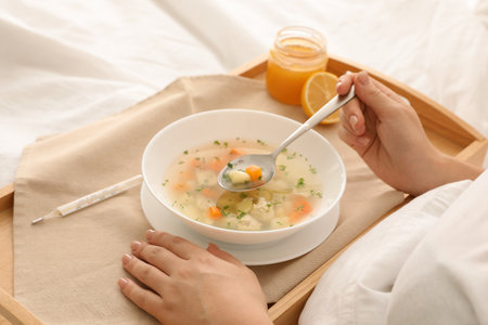 Sick woman eating fresh homemade soup to cure flu in bed at home, closeupの写真素材