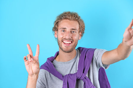 Handsome young man laughing and taking selfie on color backgroundの写真素材