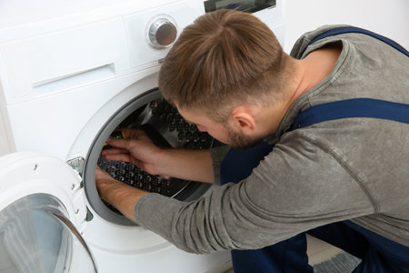 Young plumber fixing washing machine in bathroomの写真素材