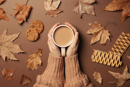 Woman in autumn sweater holding hot cozy drink on color background, top viewの写真素材