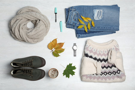 Stylish outfit and autumn leaves on white wooden background, flat lay. trendy warm clothesの写真素材