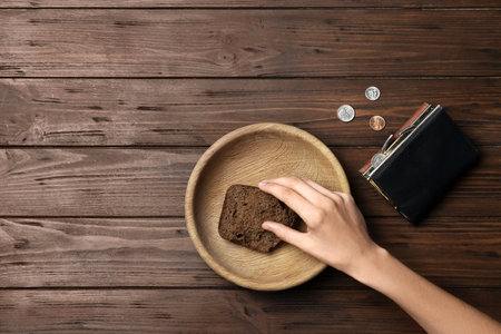 Poor woman with rye bread, wallet and coins at wooden table, space for textの写真素材