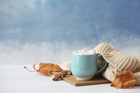Composition with hot cozy drink in cup and autumn clothing on tableの写真素材