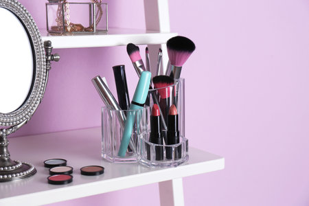 Organizer with cosmetic products for makeup on shelf near color wallの写真素材