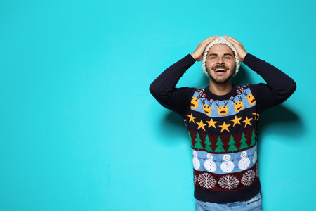 Young man in Christmas sweater and knitted hat on color background. Space for textの写真素材