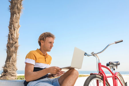 Attractive man with laptop and bike outdoors on sunny dayの写真素材