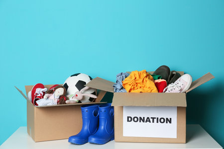Donation boxes with clothes, shoes and toys on table against color backgroundの写真素材