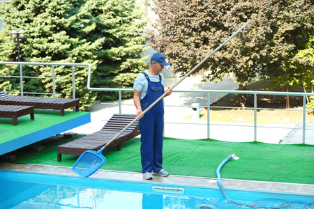 Male worker cleaning outdoor pool with scoop netの写真素材