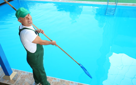 Male worker cleaning outdoor pool with scoop netの写真素材