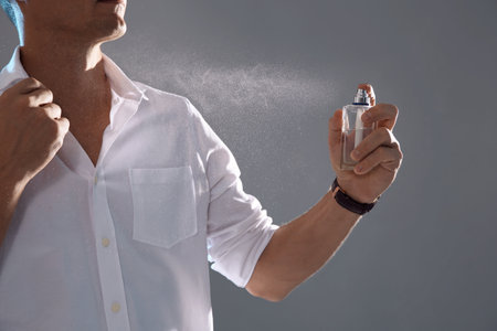 Young man spraying perfume on gray backgroundの写真素材