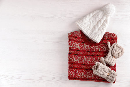 Mittens, hat and Christmas sweater with pattern on wooden background, top view. Space for textの写真素材