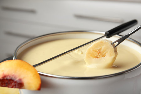 Dipping fresh banana into pot with chocolate fondue, closeupの写真素材