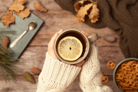 Woman in autumn sweater holding cup of hot cozy drink over wooden table, top viewの写真素材