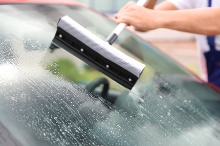 Man cleaning windshield with glass wiper, closeup. car wash serviceの写真素材