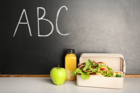Healthy food for school child in lunch box on table near blackboard with chalk written lettersの写真素材