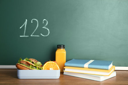 Healthy food for school child and stationery on table near chalkboard with written numbersの写真素材