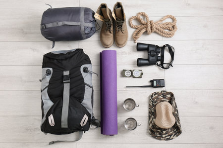 Flat lay composition with sleeping bag and camping equipment on wooden background