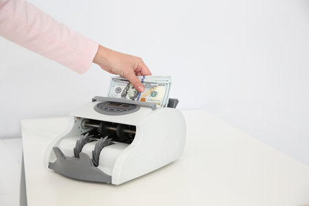 Woman putting money into counting machine on table, closeup. Space for text